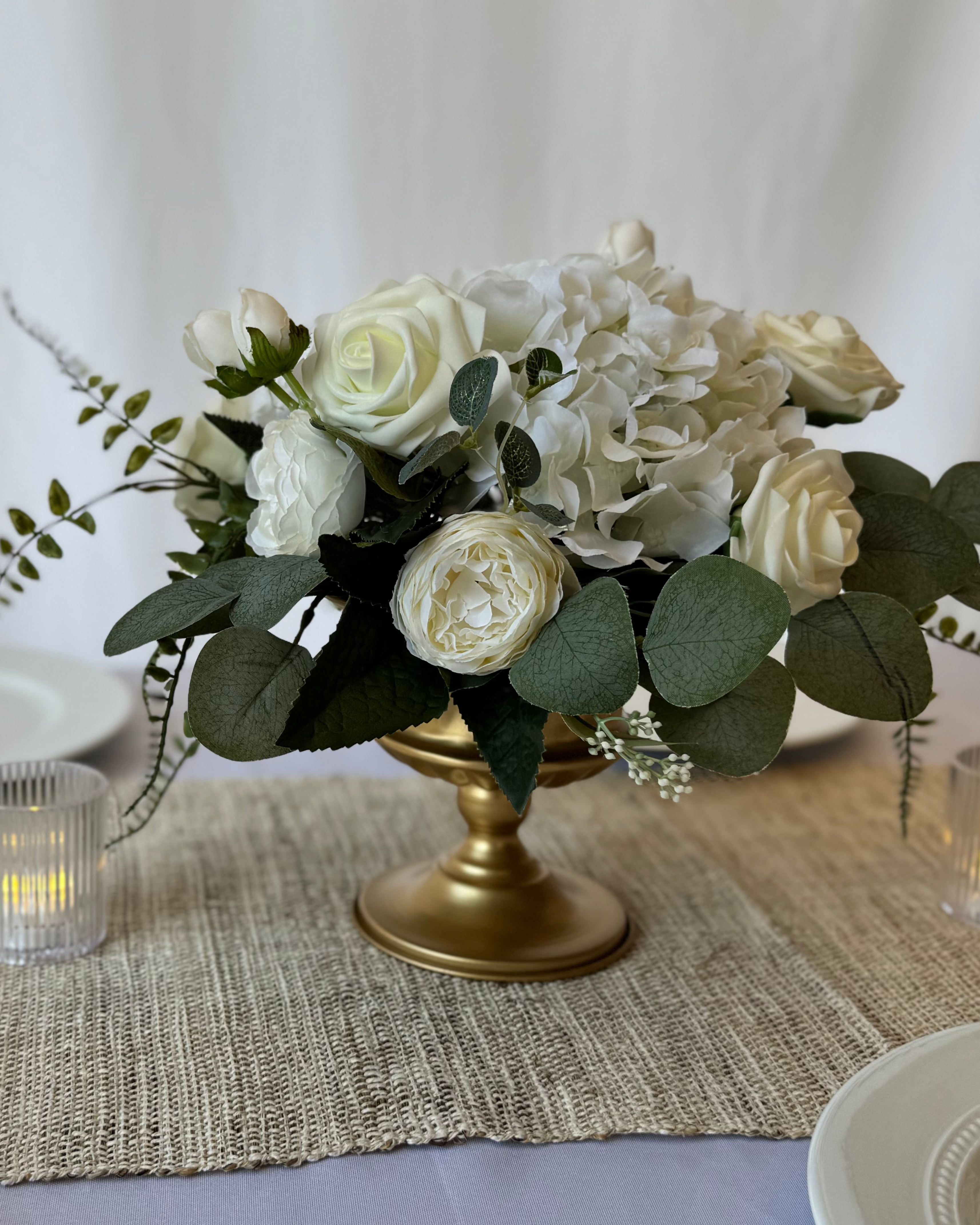 Decorative table setting with a floral arrangement, candles, and wine glasses on a neutral background.