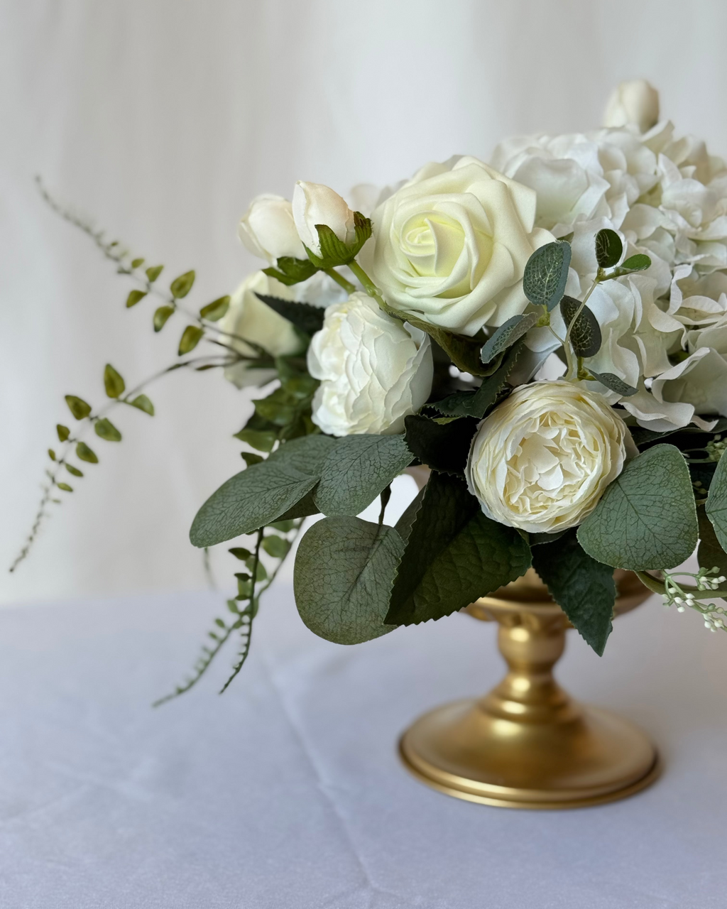 Bouquet of white flowers on a gold pedestal against a white background